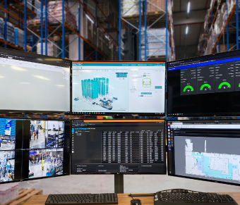 Six monitors containing data and graphics in front of warehouse storage rack